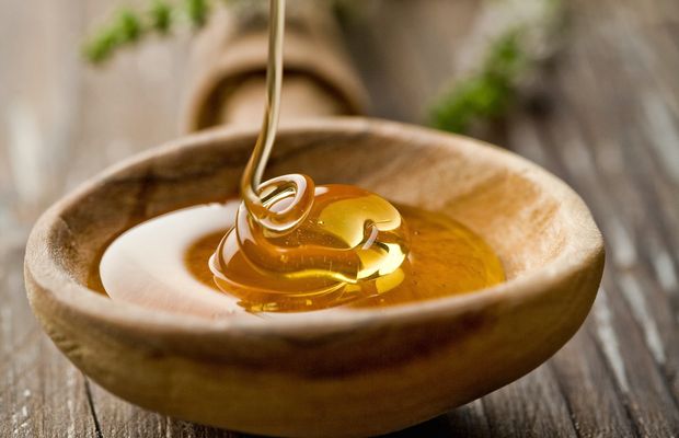 A thin stream of honey runs into a wooden spoon on a wooden table
