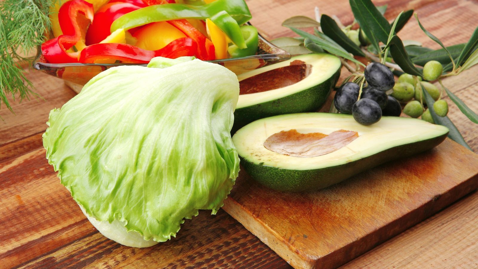 Lettuce, halved avocado, sweet peppers and olives on a wooden table