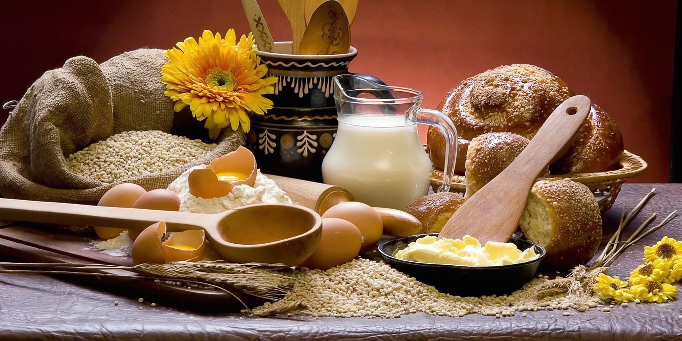 A jug of milk, eggs, a dish of butter and bread rolls on a kitchen table