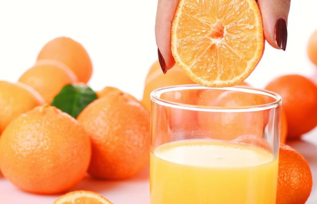 A hand squeezes half an orange over a glass of fresh juice